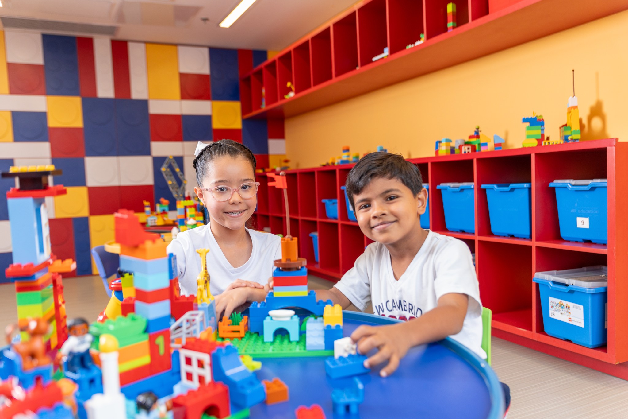 Dos estudiantes en el salón de lego, sentados y sobre la mesa varias figuras hechas de lego de colores