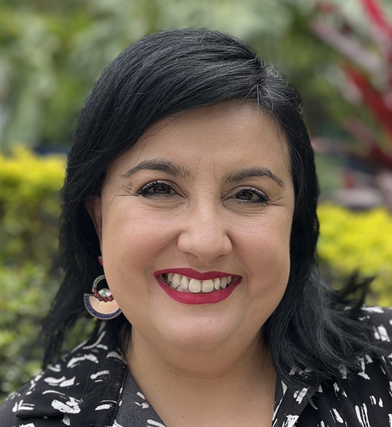 Mujer sonriendo mientras mira a la cámara, con camisa negra y apliques blancos