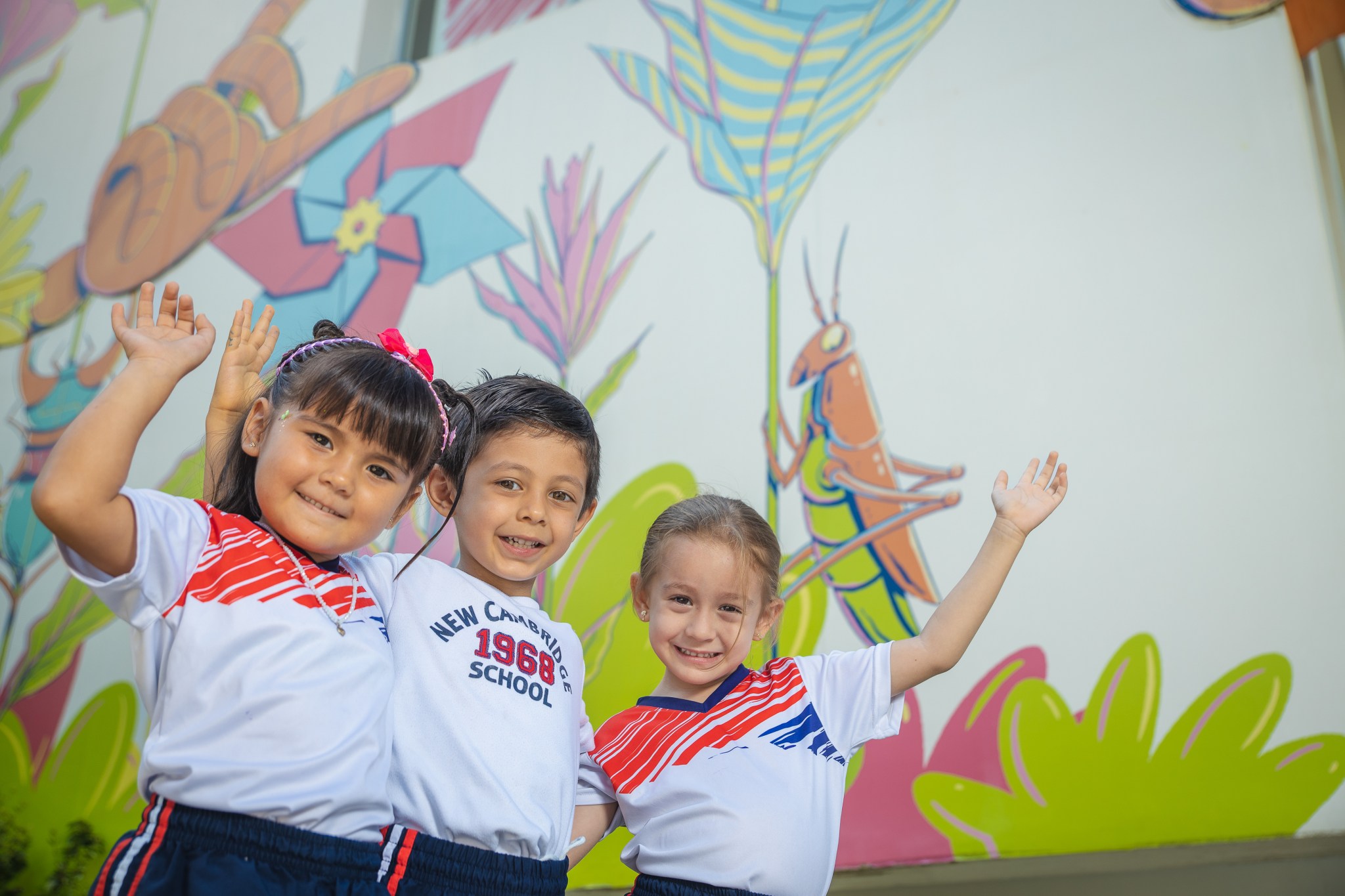 Tres estudiantes de Early Years, en plano medio, abrazados y sonriendo a la cámara, en plano contrapicado