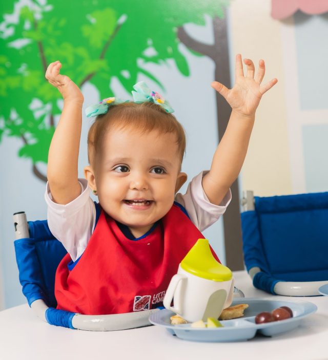 Estudiante de Early Years en el comedor, con los brazos arriba.